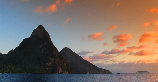 Dramatic Caribbean sunset casting golden light over the Piton mountains and ocean horizon, evoking serenity and island romance | East Winds Luxury Resort Saint Lucia