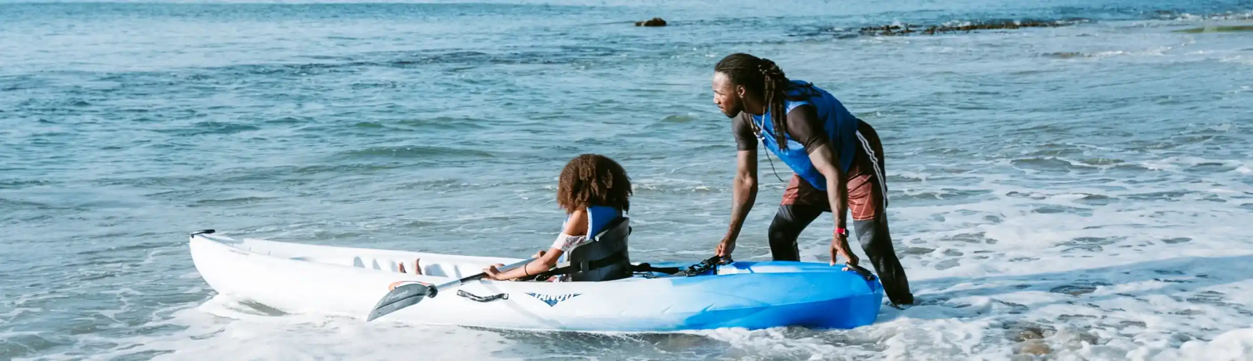 Man launching kayak with child into the sea on a sunny day | East Winds Luxury Resort Saint Lucia
