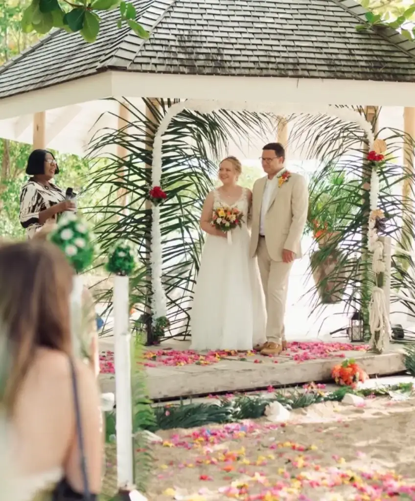 Wedding ceremony under a gazebo with floral decorations and a smiling couple.