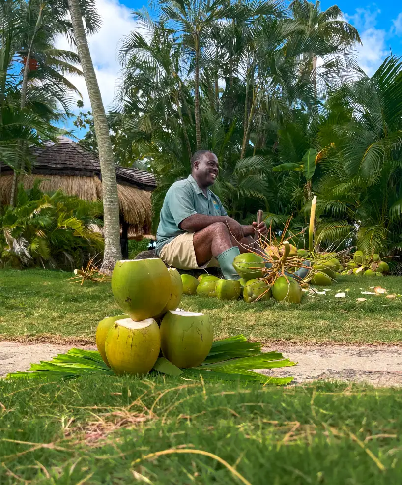 Local artisan cutting fresh coconuts at East Winds Resort, offering guests refreshing coconut water