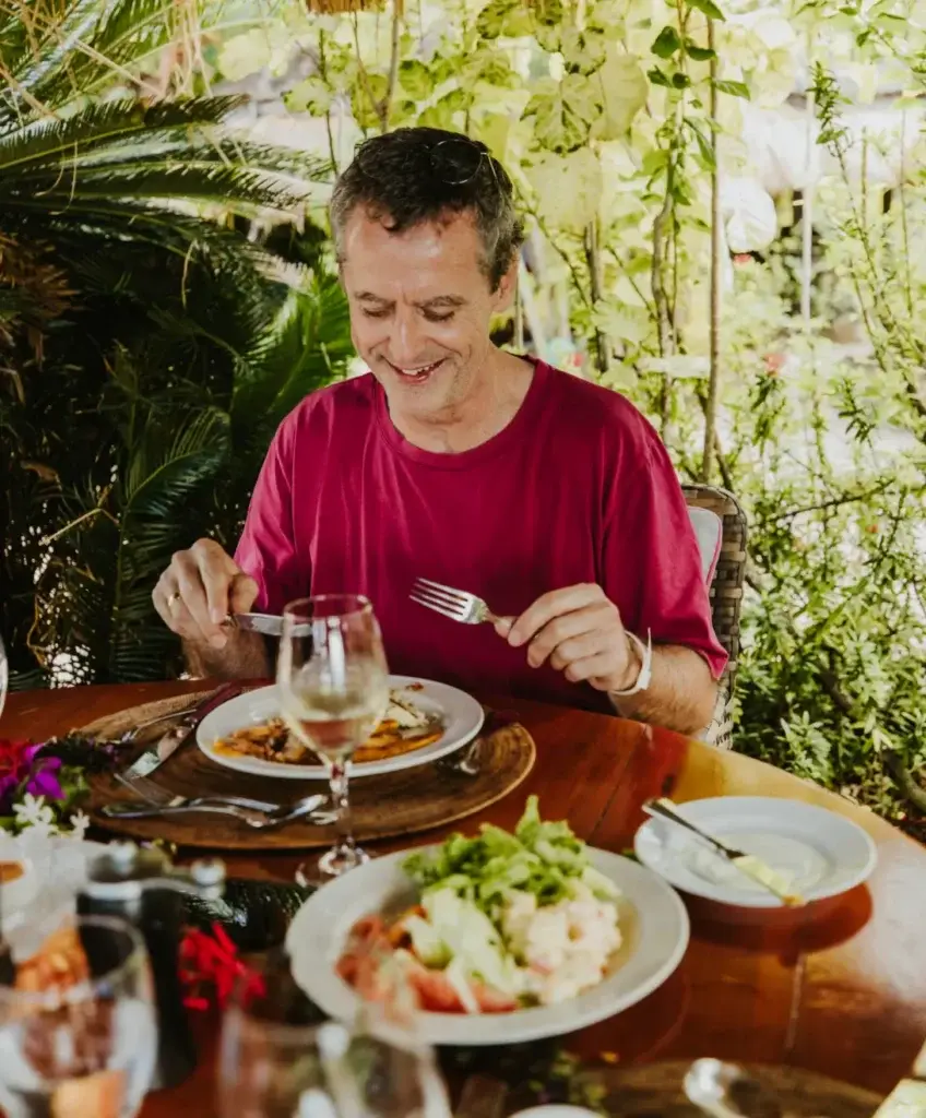 Man enjoying a meal outdoors with fresh dishes and greenery surrounding the table.