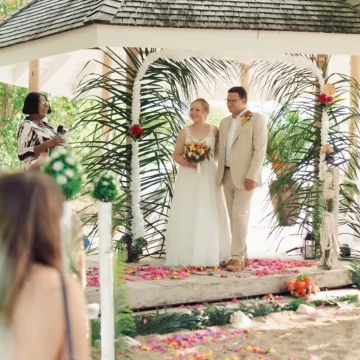 Wedding ceremony under a gazebo with floral decorations and a smiling couple.